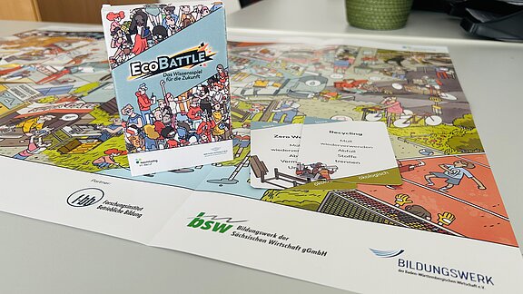 Foto von Spiel EcoBattle dass auf dem Wimmelbildposter steht, beides liegt auf einem Tisch